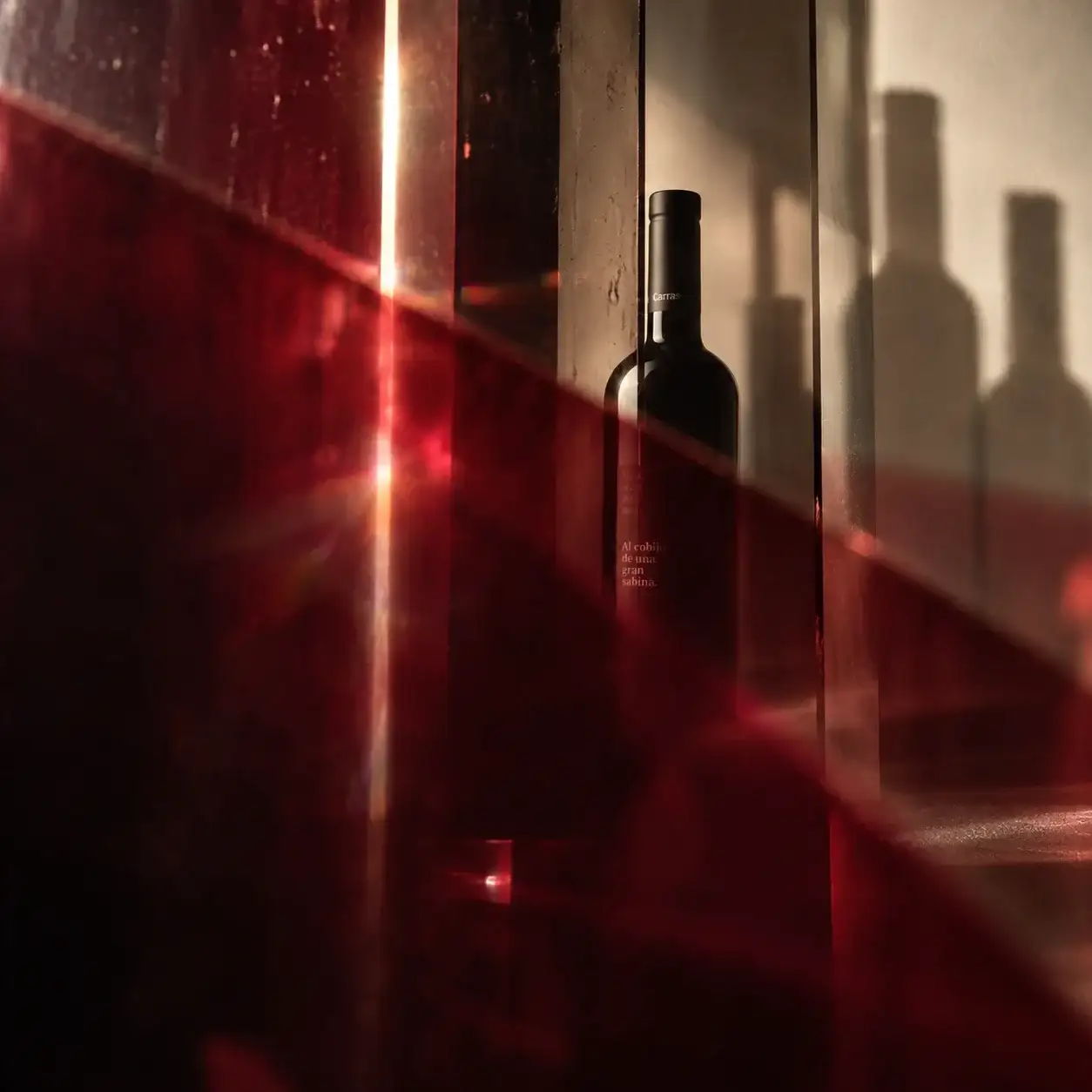 Botella de Carrascas «Al cobijo de una gran sabina» entre cristales y luz roja.