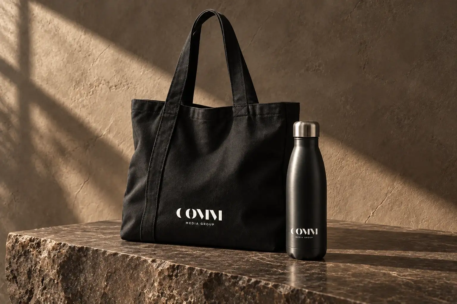Bolsa de tela y botella negras con el logotipo de COMM Media Group sobre piedra.