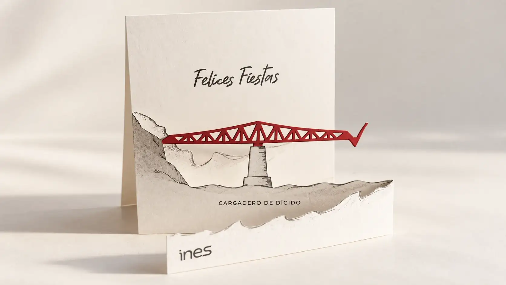 Felicitación de Navidad de INES en papel troquelado por capas con el Cargadero de Dícido en rojo y el texto «Felices Fiestas».