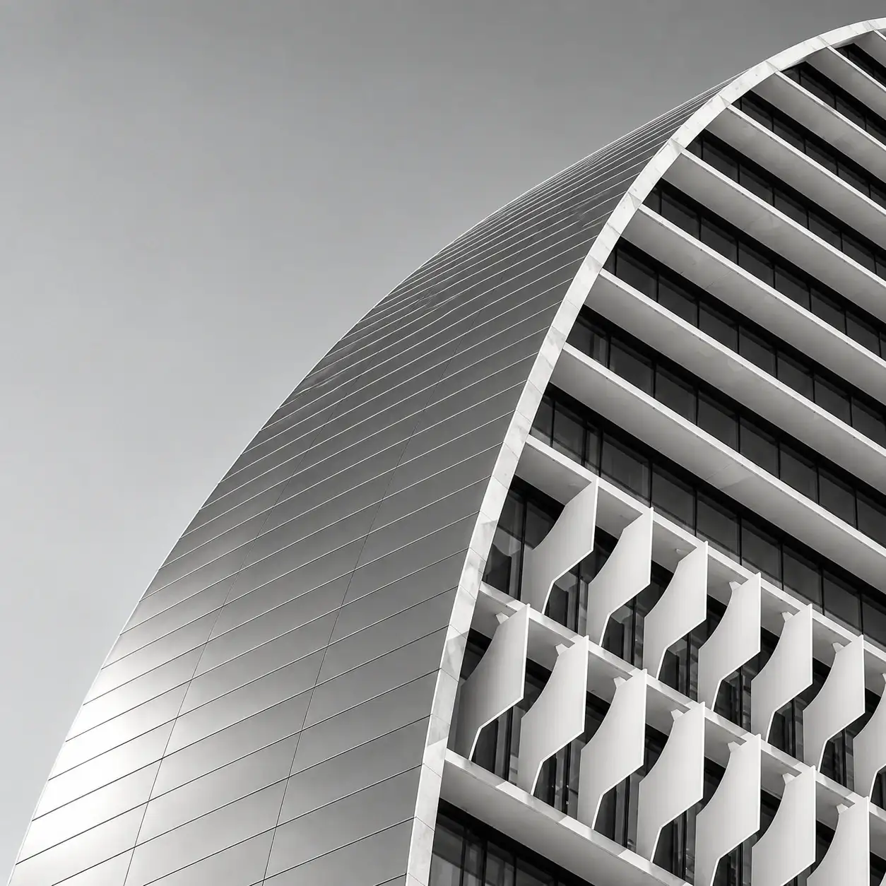 Fachada curva de un edificio de oficinas en blanco y negro, con lamas blancas.