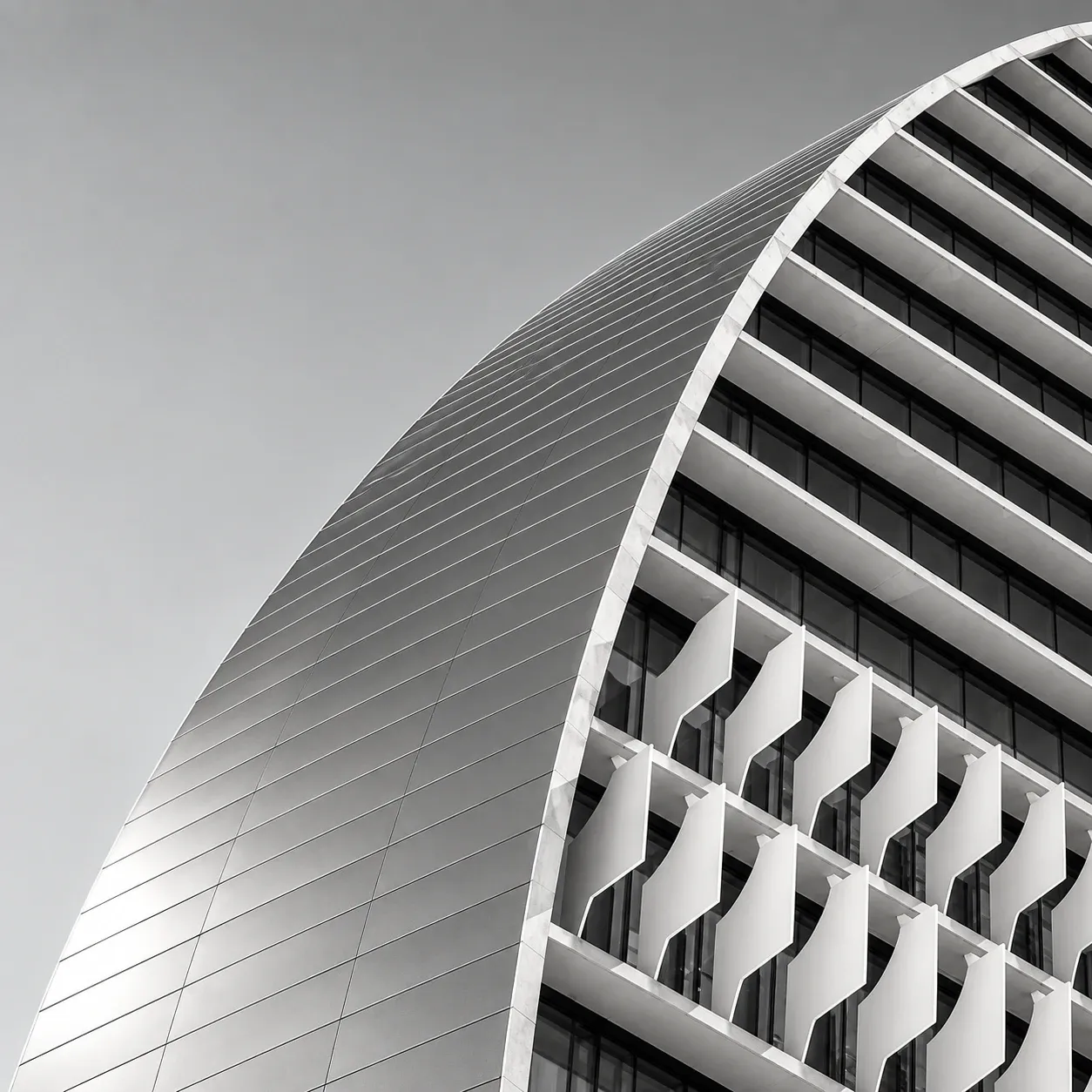 Fachada curva de un edificio de oficinas en blanco y negro, con lamas blancas.